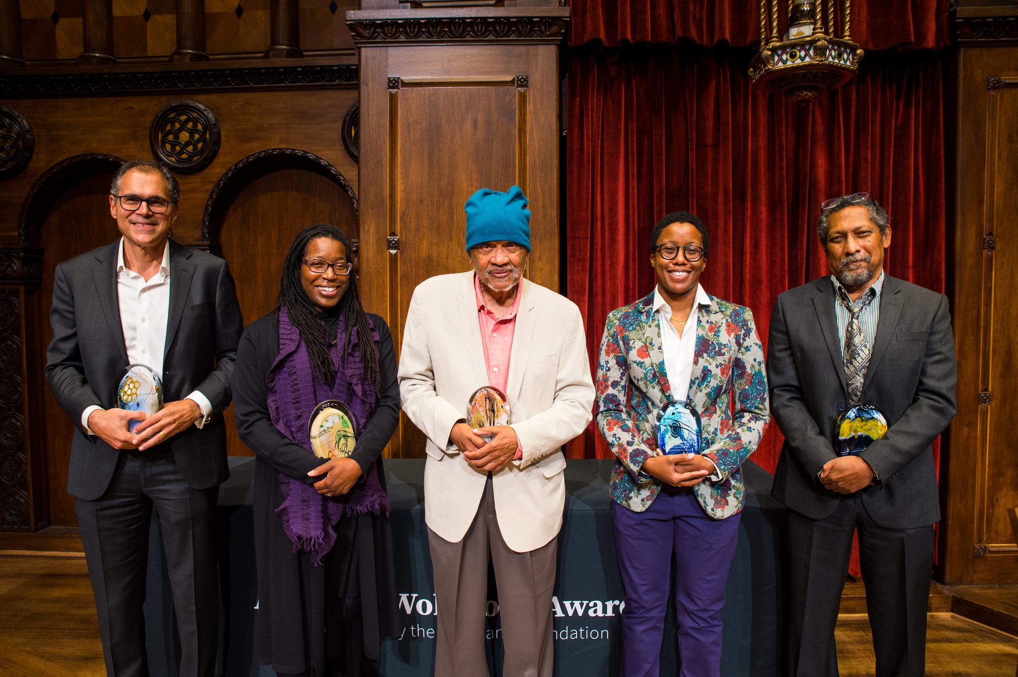 Tiya wearing black with a purple scarf holding her colorful award, standing with the other award winners.