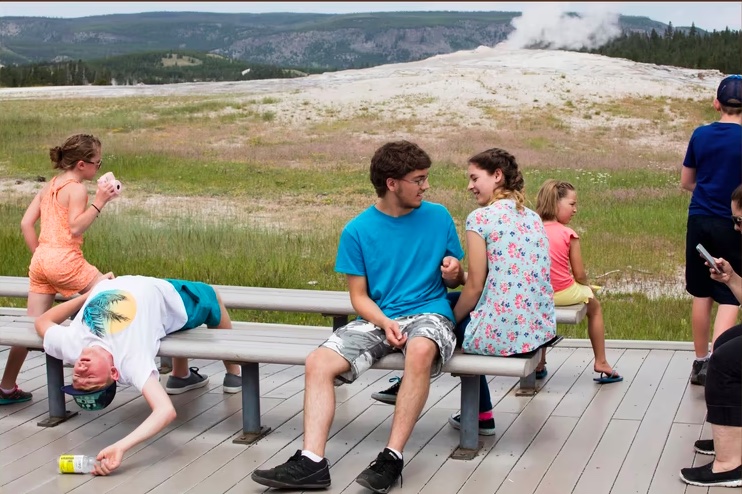 Kids sitting on benches in Yellowstone National Park with a geyser steaming in the background