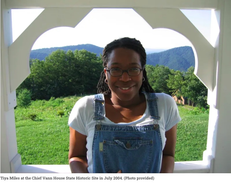 tiya wearing overalls smiling in front of a lush green field